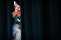 Terrifying clown hiding behind black curtains, space for text. Halloween party costume Royalty Free Stock Photo