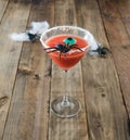 Terrifying red cocktail with spider on wooden background for Halloween with decoration. Photo square format