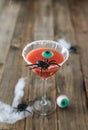 Terrifying red cocktail with spider on wooden background for Halloween with decoration. Vertical photo.