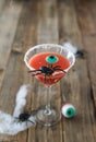 Terrifying red cocktail with spider on wooden background for Halloween with decoration. Vertical photo