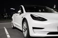 Tesla electric car parked in city parking at night. Front view, design and appearance of white electric car of Tesla Motors