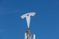 Tesla logo sign on a pole high in the blue sky.