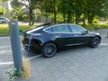 Tesla model electric car charging batteries at plug in charge station in leafy green suburb inthe Netherlands