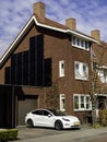 Tesla Model 3 Electric EV Car Charging at Home in Front of Modern Low Energy House with Solar Panels.