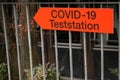 Test station Covid-19 signpost in German language in orange color and in the shape of arrow showing the direction to the testing c