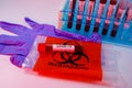 Test tube for covid-19 on a biohazard transportation bag and a blue surgical glove, blood test tubes rack in the background