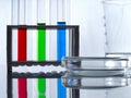 Test tubes with blue, green and red liquid in a tube rack, measuring cup and a petri dish on a white table and white background. Royalty Free Stock Photo