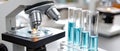 Test tubes with blue liquid stand next to a modern microscope on a table in a laboratory setting with a simple background Royalty Free Stock Photo