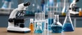 Test tubes with blue liquid stand next to a modern microscope on a table in a laboratory setting with a simple background Royalty Free Stock Photo