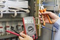 Tester and wire cutters in hands of electrician against electric control panel of automation equipment