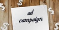 Text Ad Campaign on text, paper signs of dollar on wood table. Business concept