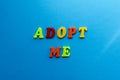 Text adopt me from plastic colored letters on blue paper background