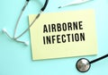 The text AIRBORNE INFECTION is written in a yellow pad that lies next to the stethoscope on a blue background.