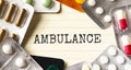 Text AMBULANCE on a white background. Nearby are various medicines. Medical concept