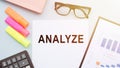 The text ANALYZE on office desk with calculator, markers, glasses and financial charts