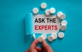 The text `ask the experts` appearing behind torn blue paper. White pills and male hand. Beautiful blue and white background Royalty Free Stock Photo
