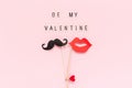 Text Be my Valentine and couple paper mustache, lips props fastened clothespin heart on stick on pink paper background
