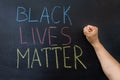 The text Black lives matter, on a chalkboard. A man`s fist against a chalkboard