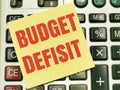 Text BUDGET deficit written on yellow paper note on calculator.