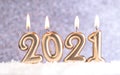 Text 2021, burning melting candles in the snow, on a blurred silver background with bokeh. Christmas and New Years concept. Royalty Free Stock Photo