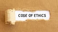 Text Code of Ethics appearing behind torn brown paper