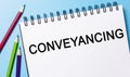 Text Conveyancing on a white notepad with pencils on a blue background. Business concept
