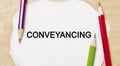 Text Conveyancing on a white notepad with pencils on a wooden background. Business concept