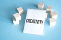 Text CREATIVITY on white notepad with cube block, stock concept