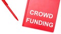 The text CROWD FUNDING is written on a red notepad near a red pen on a white table in the office. Business concept Royalty Free Stock Photo