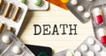 Text DEATH on a white background. Nearby are various medicines. Medical concept