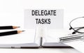 Text DELEGATE TASKS on paper card,pen, pencils, glasses,financial documentation on table - business concept
