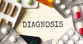 Text DIAGNOSIS on a white background. Nearby are various medicines. Medical concept