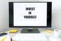 Text displayed on the monitor, Invest in Yourself. A desk with a keyboard, office accessories and a cup of coffee. The concept o