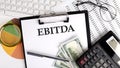 Text EBITDA on Office desk table with keyboard, dollars,calculator ,supplies,analysis chart on the white background Royalty Free Stock Photo