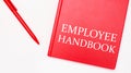 The text EMPLOYEE HANDBOOK is written on a red notepad near a red pen on a white table in the office. Business concept Royalty Free Stock Photo