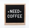 Text in english spelling `Need Coffee` with smiley face emojis on black felt board in a wooden frame. Letter Board on white