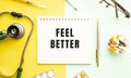 Text FEEL BETTER on notebook with stethoscope and pen on yellow background.