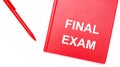 The text FINAL EXAM is written on a red notepad near a red pen on a white table in the office. Business concept Royalty Free Stock Photo