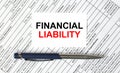 Text Financial Liability written on a business card lying on financial tables with a blue metal pen