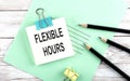 Text FLEXIBLE HOURS on the short note with pencils on the wooden background