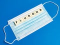 Text flurona made of square letter tiles with medical mask against blue background.