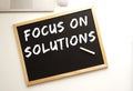 Text FOCUS ON SOLUTIONS written in chalk on a slate board. Office desk. Royalty Free Stock Photo
