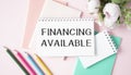Funding is available on the sheet next to a flower, notepad, colored pencils on a pink background Royalty Free Stock Photo