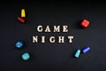 Text GAME NIGHT spelled out in wooden letter. Surrounded by dice, dominoes other game pieces on black background. Table games. Royalty Free Stock Photo