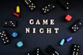 Text GAME NIGHT spelled out in wooden letter. Surrounded by dice, dominoes other game pieces on black background. Table games. Royalty Free Stock Photo