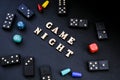 Text GAME NIGHT spelled out in wooden letter. Surrounded by dice, dominoes other game pieces on black background. Table Royalty Free Stock Photo