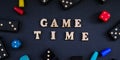 Text GAME TIME spelled out in wooden letter. Surrounded by dice, dominoes other game pieces on black background. Table Royalty Free Stock Photo