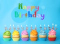 Text Happy Birthday and delicious cupcakes with burning candles on blue background Royalty Free Stock Photo