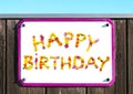 HAPPY BIRTHDAY sign made of yellow pink red and orange flowers collage, pink sign frame, wooden wall, turquoise sky Royalty Free Stock Photo