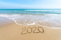 Text 2020 Happy New Year on the beach with waves and clear blue sea. 2020 numbers on the coast. Hand written messages in sand on a